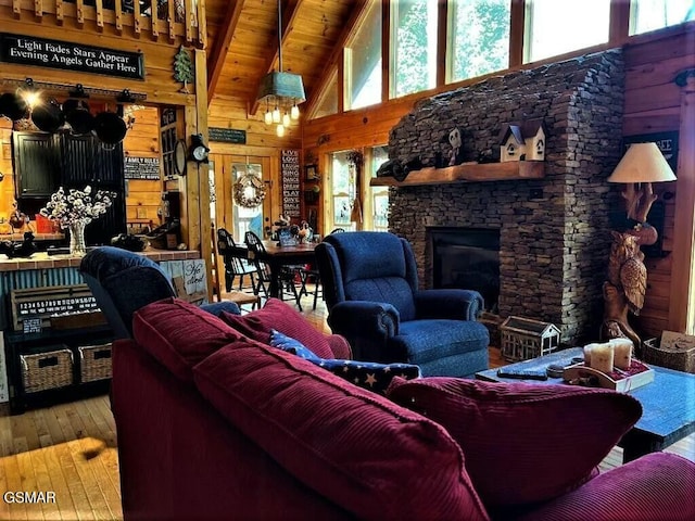 living area featuring beam ceiling, hardwood / wood-style flooring, wooden walls, a stone fireplace, and wooden ceiling