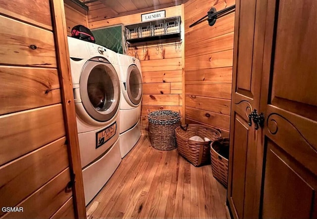 clothes washing area featuring independent washer and dryer, laundry area, wooden walls, and light wood-type flooring