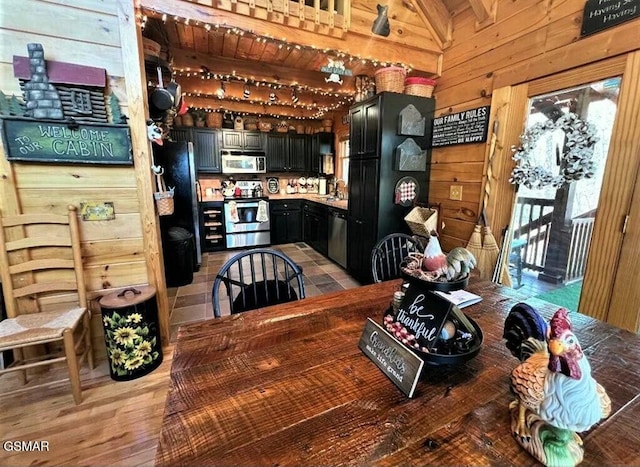 kitchen with light wood-style flooring, a sink, wooden walls, appliances with stainless steel finishes, and dark cabinets