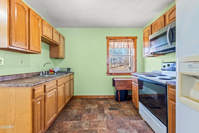 kitchen with stone finish floor, a sink, dark countertops, white appliances, and baseboards