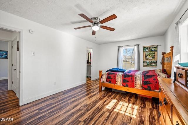 bedroom with a walk in closet, baseboards, wood finished floors, a textured ceiling, and a ceiling fan