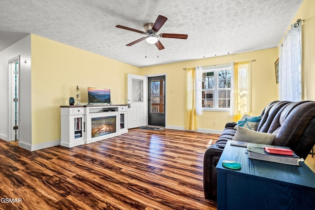 living room with baseboards, ceiling fan, wood finished floors, a glass covered fireplace, and a textured ceiling