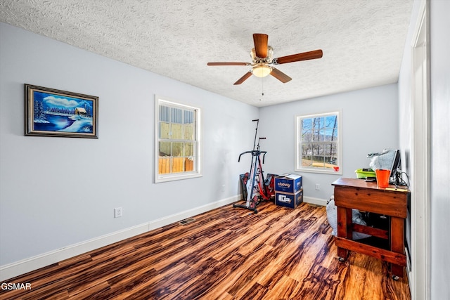 exercise area featuring a textured ceiling, baseboards, a ceiling fan, and wood finished floors