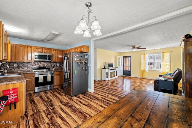 kitchen featuring dark wood-style floors, a sink, decorative backsplash, stainless steel appliances, and open floor plan