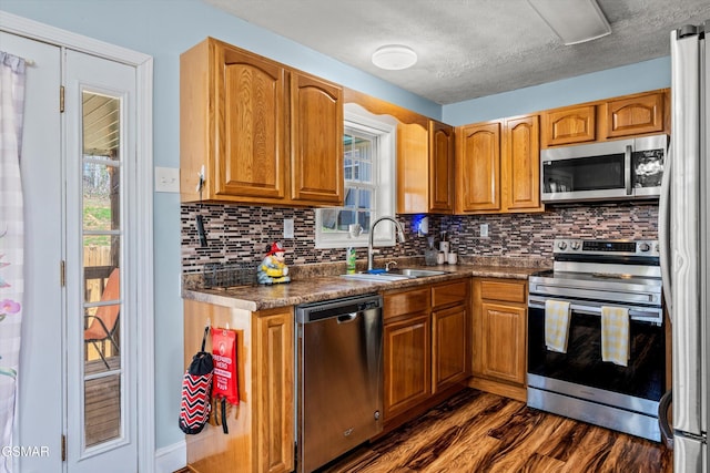 kitchen with dark wood finished floors, brown cabinetry, appliances with stainless steel finishes, and a sink