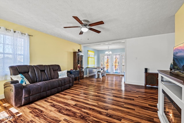 living area featuring baseboards, a textured ceiling, wood finished floors, and ceiling fan with notable chandelier