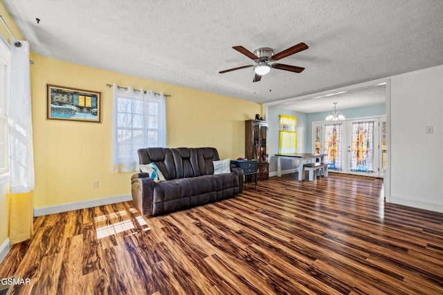 living area featuring ceiling fan with notable chandelier, wood finished floors, baseboards, and a textured ceiling