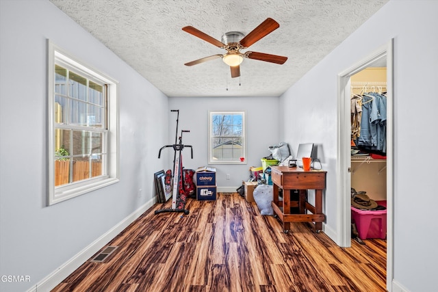 workout room featuring visible vents, baseboards, wood finished floors, a textured ceiling, and a ceiling fan