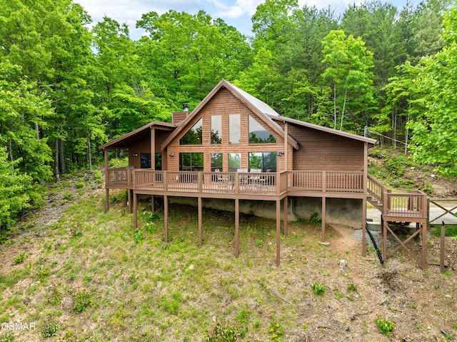rear view of property featuring a wooden deck, a wooded view, and a chimney