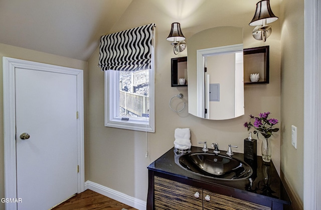 bathroom with baseboards, vanity, wood finished floors, and lofted ceiling