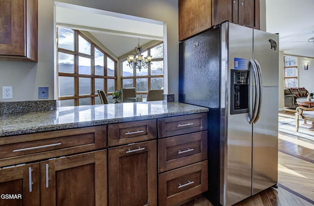 kitchen featuring stone countertops, dark brown cabinetry, stainless steel refrigerator with ice dispenser, wood-type flooring, and ceiling fan with notable chandelier
