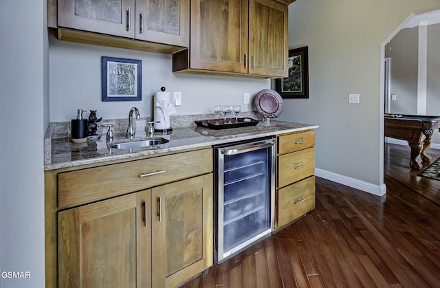 kitchen with light stone countertops, dark wood-type flooring, a sink, beverage cooler, and baseboards
