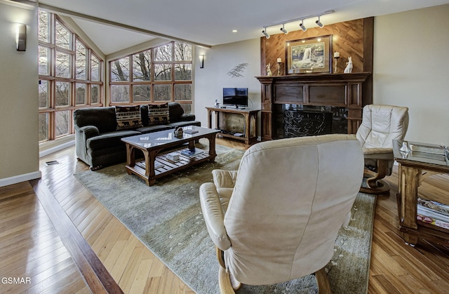 living room featuring a fireplace, rail lighting, visible vents, vaulted ceiling, and hardwood / wood-style flooring