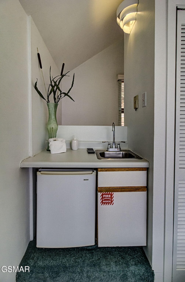 kitchen featuring a sink, light countertops, dishwashing machine, carpet floors, and vaulted ceiling