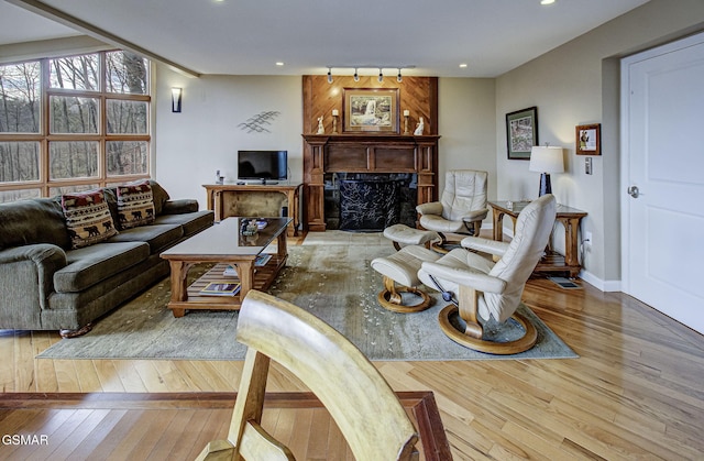 living room featuring baseboards, a high end fireplace, recessed lighting, wood-type flooring, and rail lighting