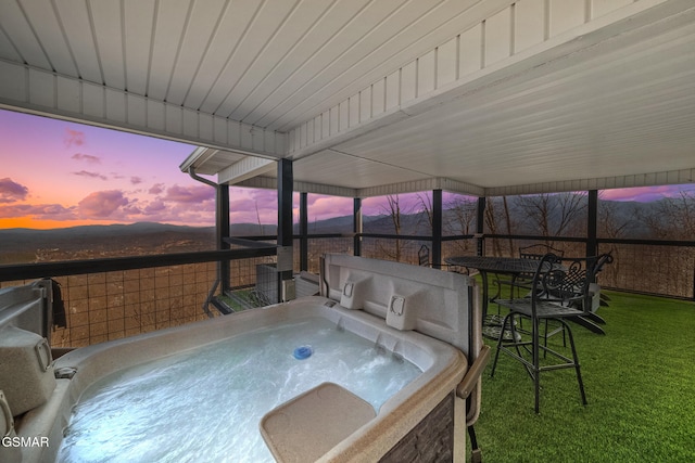 patio terrace at dusk with a lawn and a hot tub