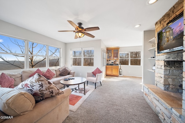 living room featuring a stone fireplace, light colored carpet, and ceiling fan