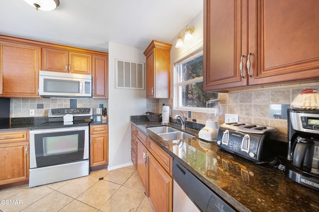 kitchen featuring dark stone countertops, stainless steel appliances, sink, and light tile patterned floors