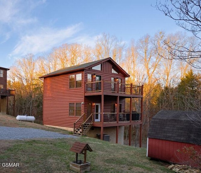 back of property featuring a wooden deck, a lawn, a storage shed, an outdoor structure, and log veneer siding