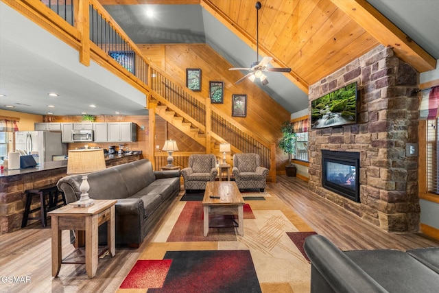 living area with light wood finished floors, stairs, wood walls, a fireplace, and high vaulted ceiling