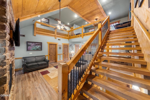 staircase with ceiling fan, a towering ceiling, wood finished floors, and wood ceiling