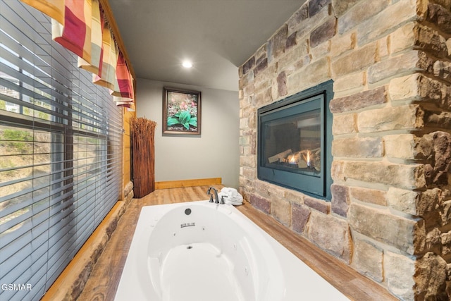 bathroom featuring a jetted tub, wood finished floors, and a stone fireplace