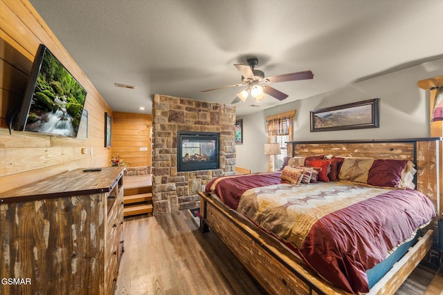 bedroom with a stone fireplace, wooden walls, a textured ceiling, and wood finished floors