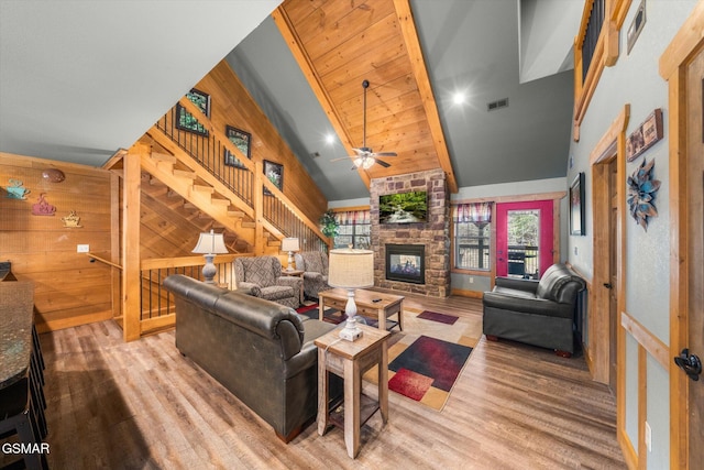 living area with wooden walls, visible vents, wood finished floors, and a stone fireplace