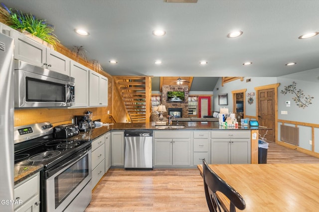 kitchen featuring a peninsula, vaulted ceiling, stainless steel appliances, light wood-type flooring, and a sink