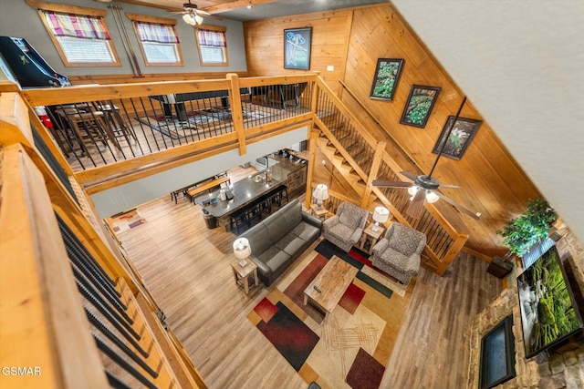 living area with ceiling fan, a high ceiling, wood walls, a fireplace, and stairs