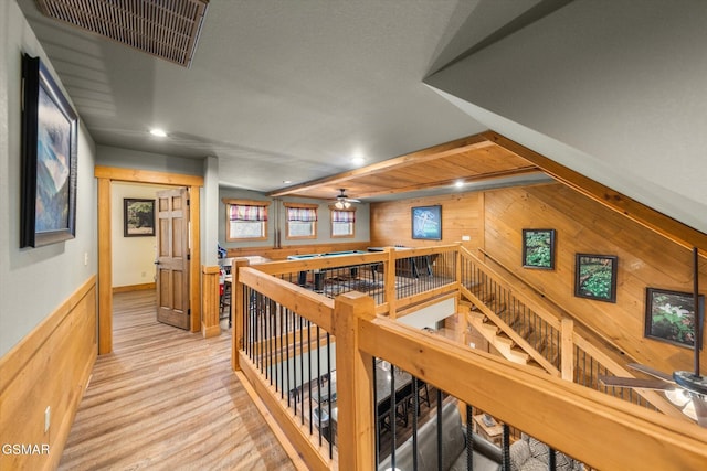 corridor featuring wooden walls, visible vents, light wood-style flooring, an upstairs landing, and recessed lighting