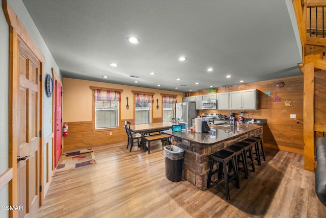 kitchen featuring a wainscoted wall, a breakfast bar area, appliances with stainless steel finishes, light wood-style floors, and wooden walls