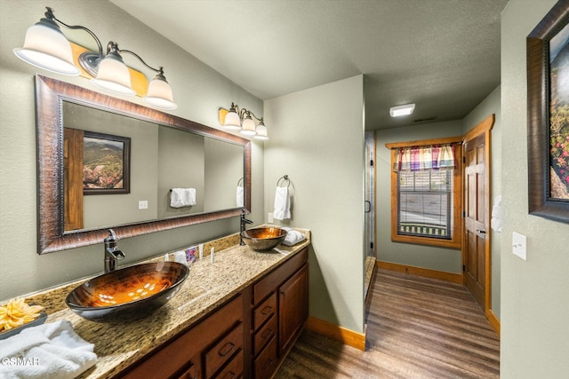 full bath featuring double vanity, wood finished floors, a sink, and baseboards