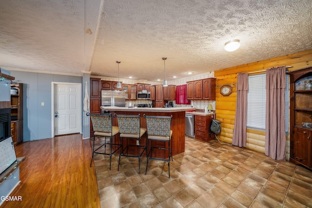 kitchen with a kitchen island, appliances with stainless steel finishes, a breakfast bar, rustic walls, and hanging light fixtures