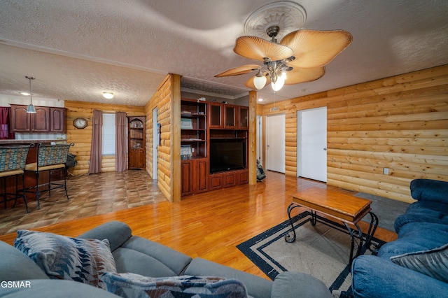 living room featuring ceiling fan, log walls, a textured ceiling, and light wood-type flooring