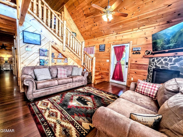 living room with a ceiling fan, wood finished floors, wood walls, a fireplace, and stairs