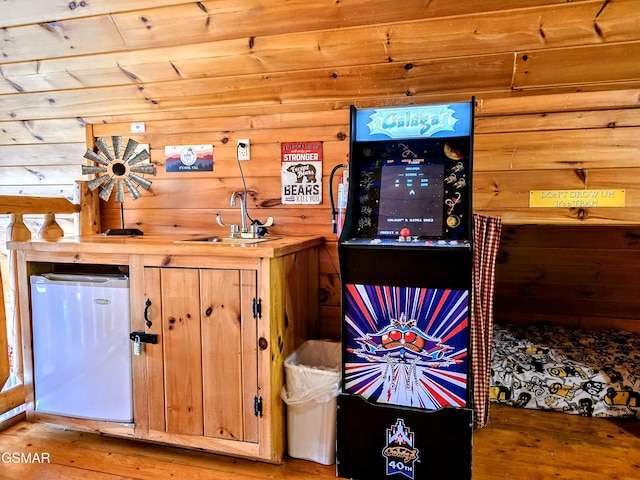 bar with a sink, refrigerator, wood walls, and hardwood / wood-style flooring