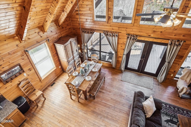 living area featuring a skylight, wooden walls, a towering ceiling, hardwood / wood-style flooring, and french doors