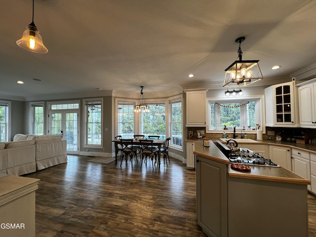 kitchen with a kitchen island, white cabinetry, open floor plan, glass insert cabinets, and pendant lighting