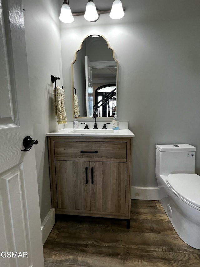 half bath featuring toilet, baseboards, wood finished floors, and vanity