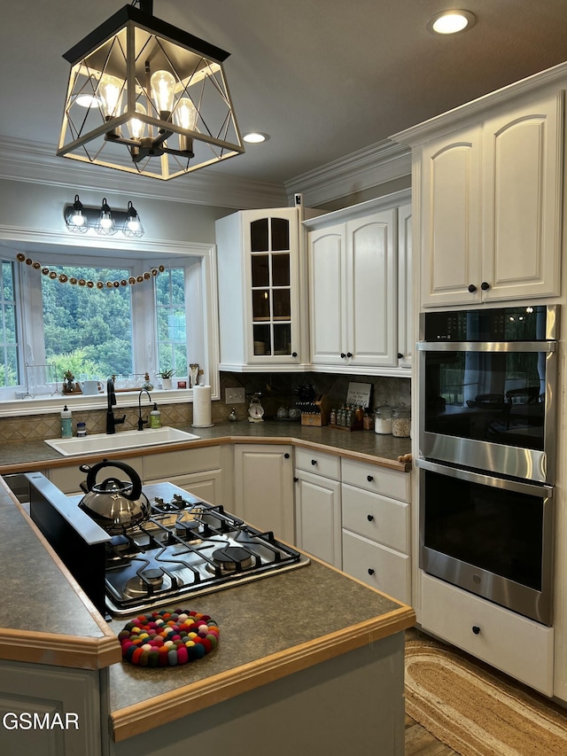 kitchen with pendant lighting, dark countertops, double oven, white cabinetry, and a sink