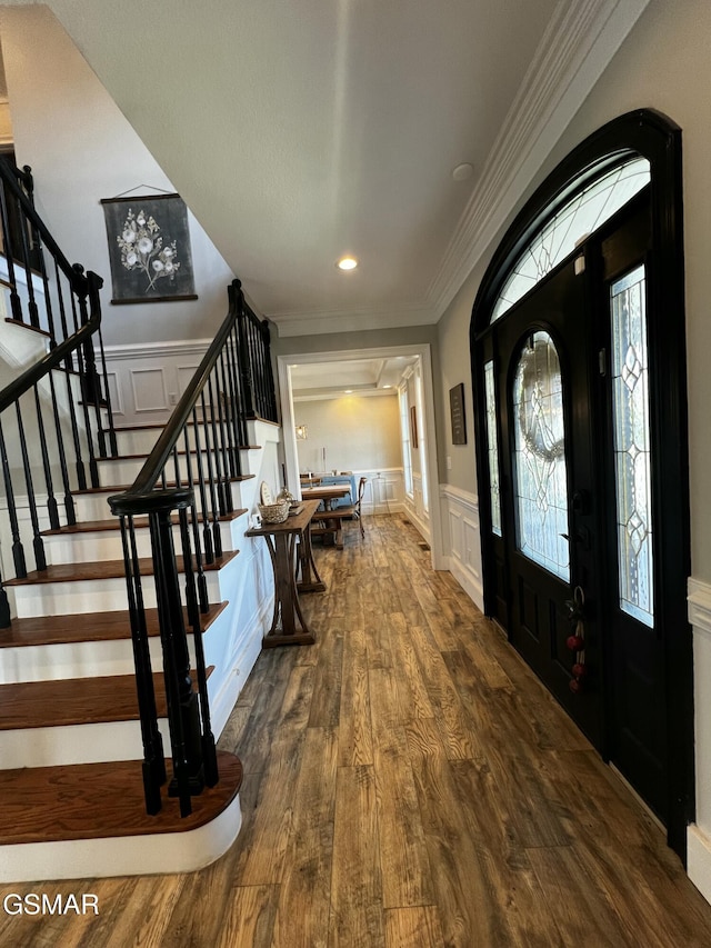 entrance foyer with a decorative wall, dark wood-style flooring, stairs, wainscoting, and crown molding