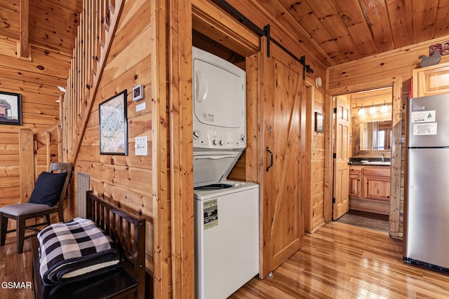 washroom featuring stacked washer / dryer, a barn door, wooden ceiling, and wooden walls