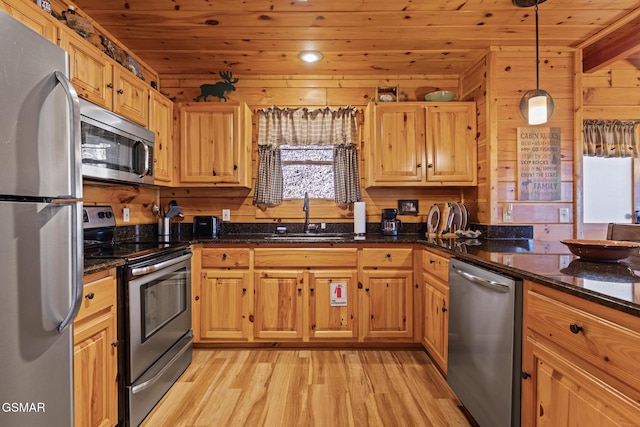 kitchen featuring sink, light hardwood / wood-style flooring, appliances with stainless steel finishes, hanging light fixtures, and wood walls