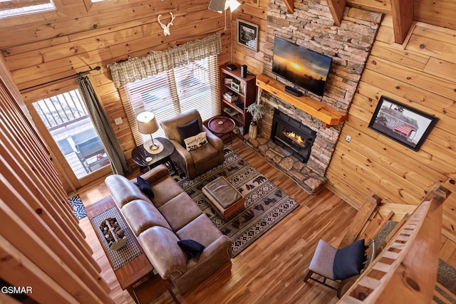 living room with wooden walls, a stone fireplace, and hardwood / wood-style floors