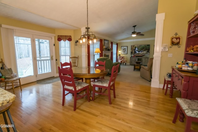 dining space with decorative columns, lofted ceiling, light wood-type flooring, a fireplace, and ceiling fan with notable chandelier