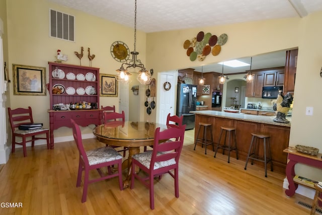 dining space featuring arched walkways, light wood-style flooring, lofted ceiling, and visible vents