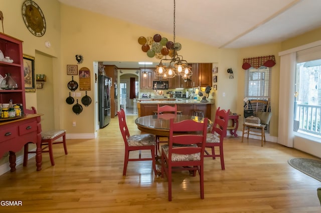 dining room with arched walkways, baseboards, light wood finished floors, and an inviting chandelier