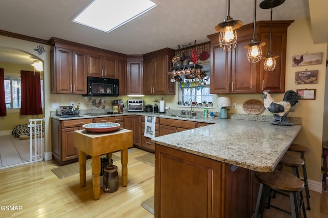 kitchen with arched walkways, a peninsula, black appliances, a kitchen bar, and a sink