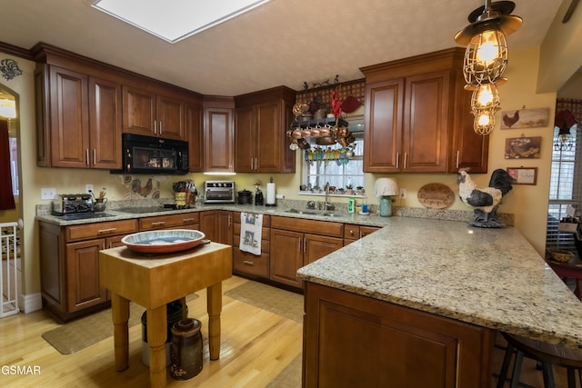 kitchen featuring pendant lighting, light wood-style flooring, a sink, a peninsula, and black appliances